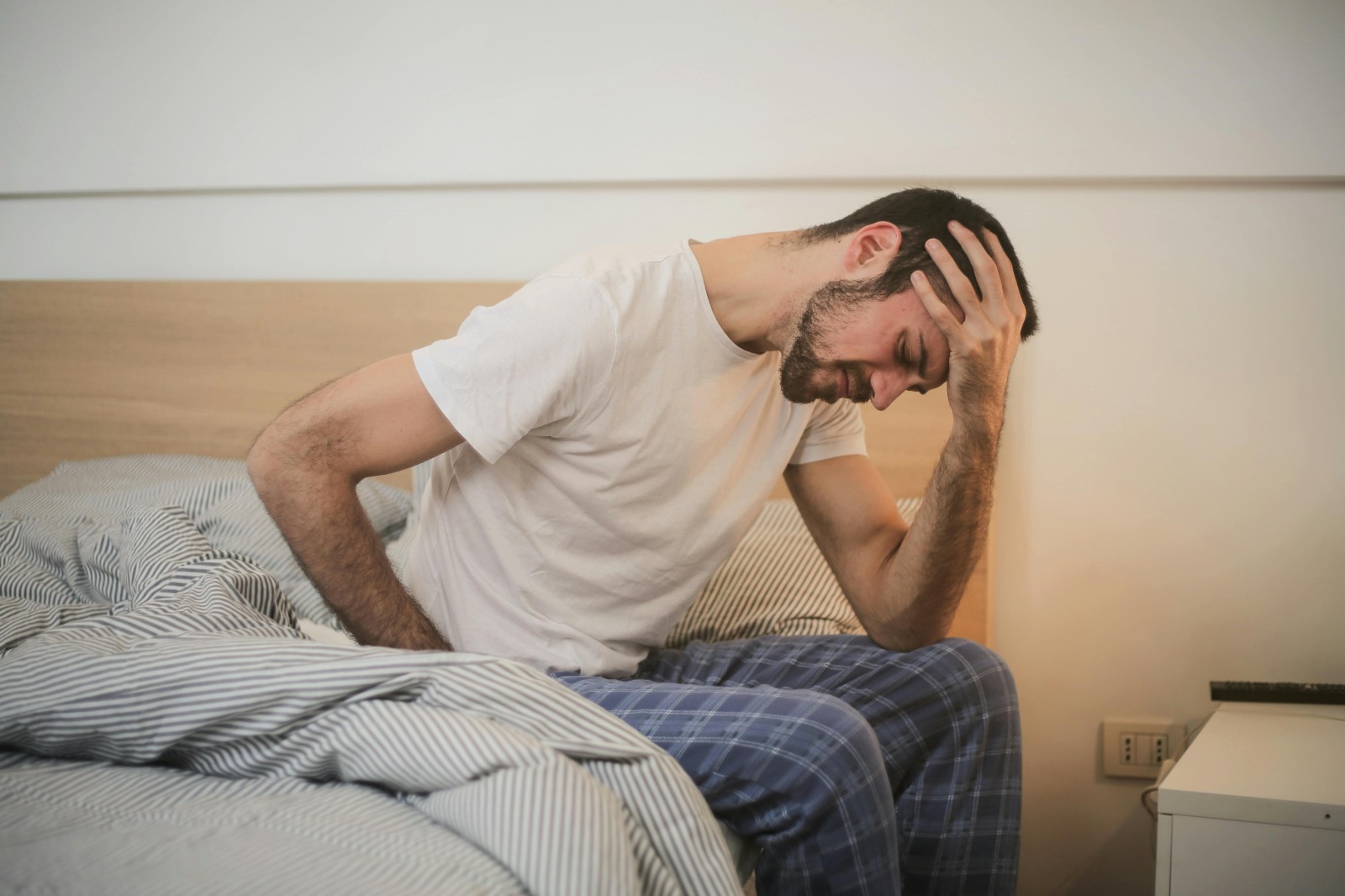 person waking up with headache in morning holding head in bed