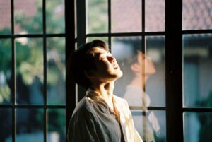 person standing near window getting morning sunlight to improve sleep cycle