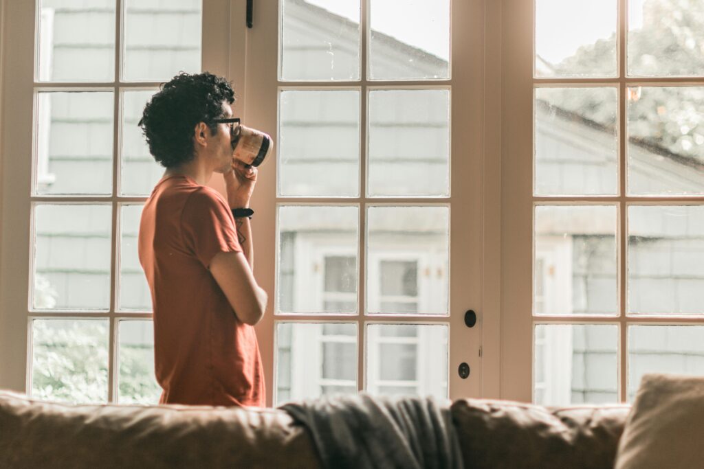 A person standing near a window enjoying morning sunlight for better sleep
